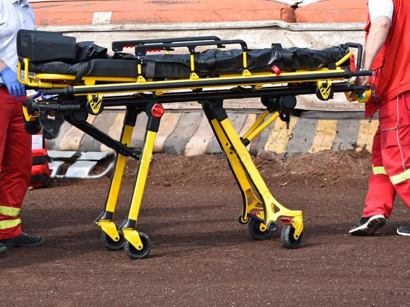 Medical responders handle a wheeled ambulance stretcher on a rough surface during an emergency response.