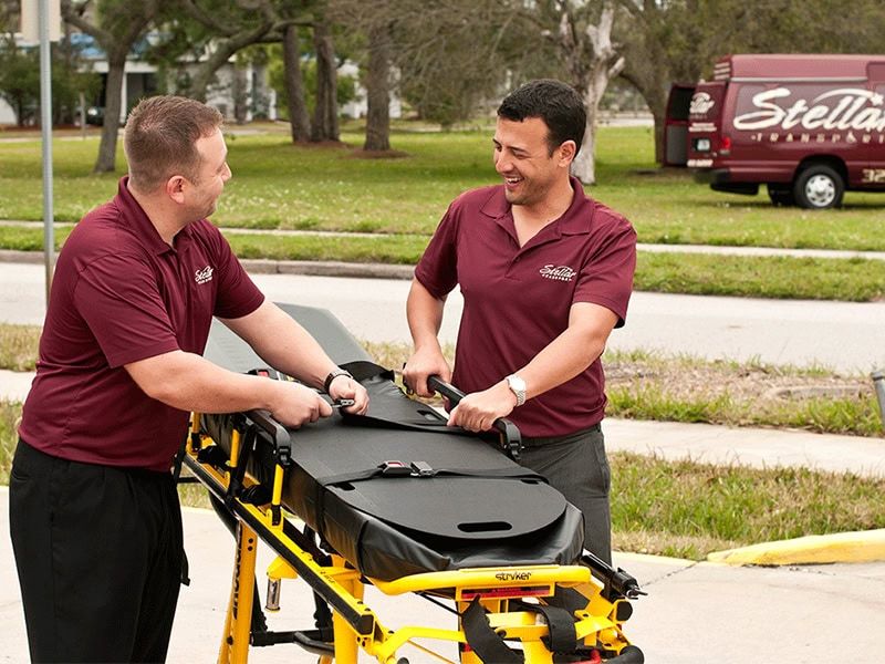 Two men in uniform adjust a stretcher outside, preparing it for transport or demonstration.