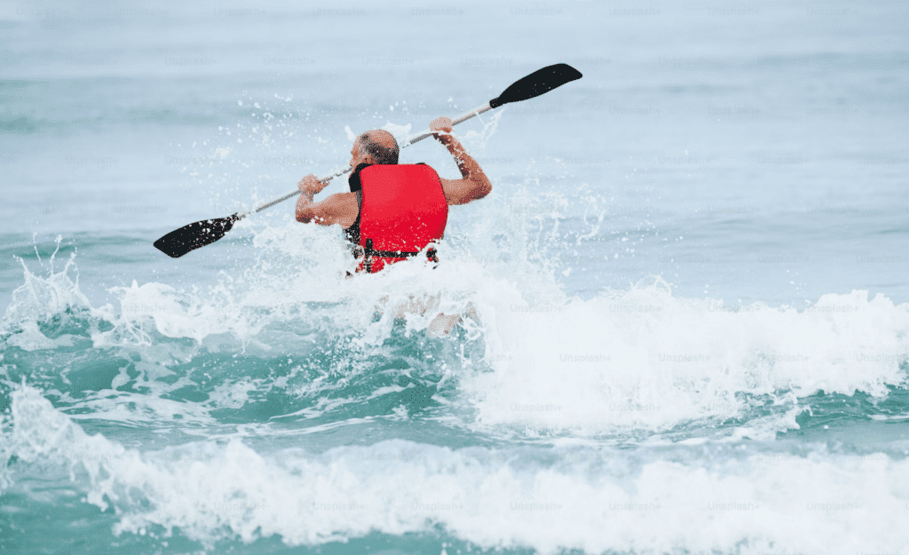 Man kayaking through waves wearing a red life jacket