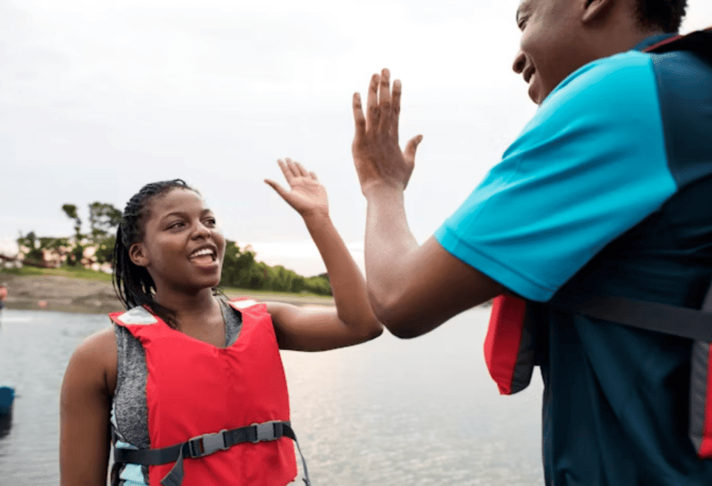 Two people wearing life jackets high-fiving near water