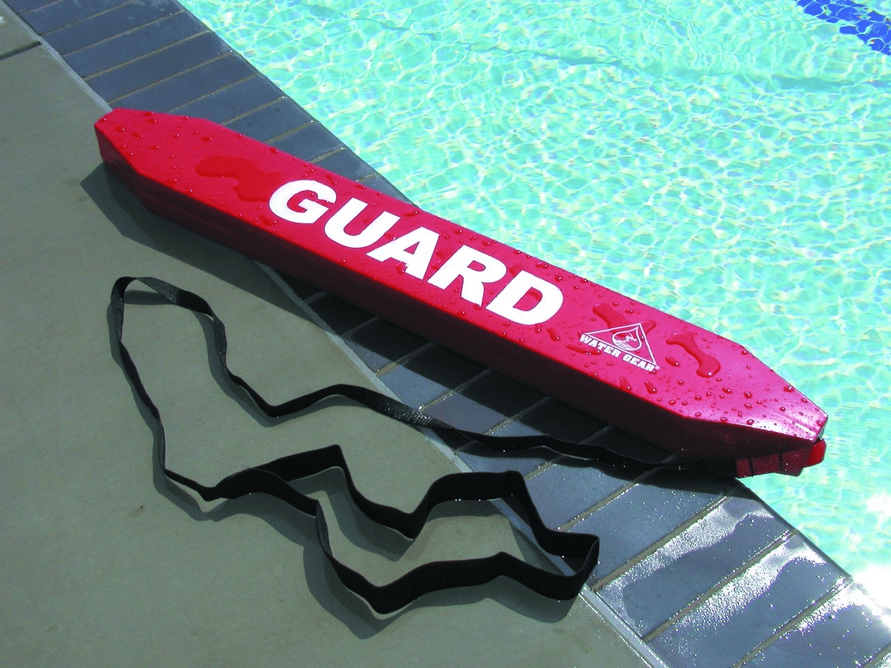 Lifeguard standing poolside holding a red rescue tube, ready for swimmer safety and emergency rescue